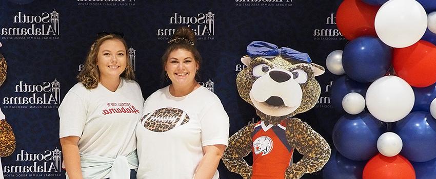 Two alumni members wearing 南 shirts standing next to Ms. Pawla断路.